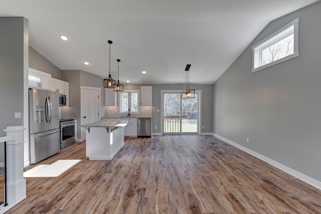 kitchen with white cabinets, light hardwood / wood-style floors, a kitchen island, and appliances with stainless steel finishes