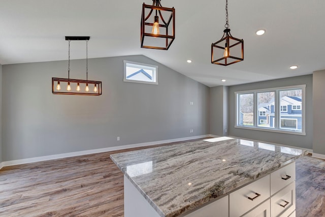 kitchen with light stone counters, vaulted ceiling, white cabinetry, light hardwood / wood-style flooring, and decorative light fixtures