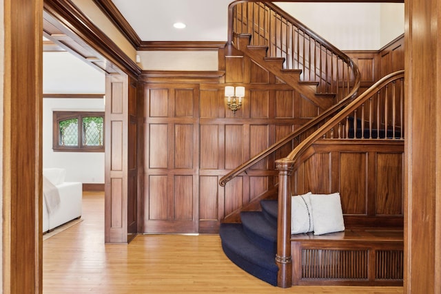 stairway with wood walls, crown molding, and wood finished floors