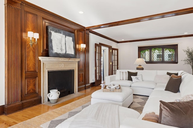 living area with a fireplace with flush hearth, recessed lighting, crown molding, and light wood-style flooring