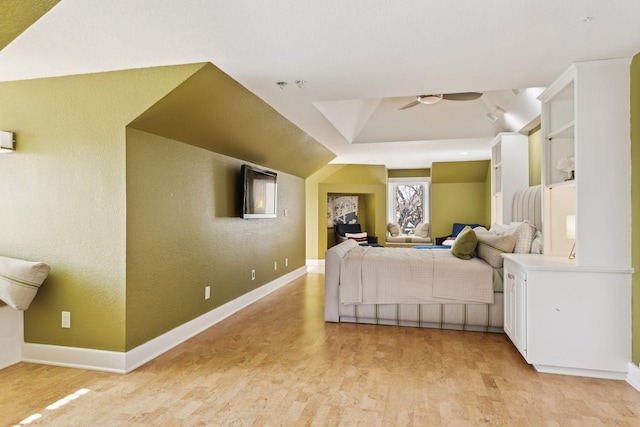 bedroom featuring a textured wall, vaulted ceiling, light wood finished floors, and baseboards