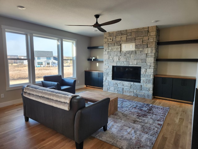 living room featuring ceiling fan, a fireplace, and light hardwood / wood-style floors