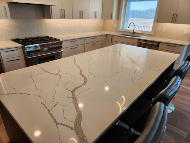 kitchen featuring a kitchen bar, sink, light stone counters, dark hardwood / wood-style floors, and stainless steel appliances