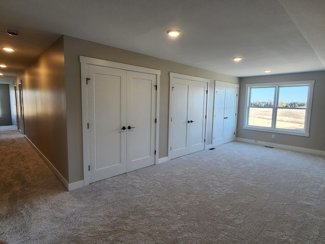 unfurnished bedroom featuring light colored carpet and multiple closets