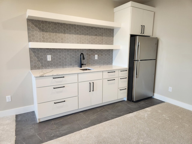 kitchen with sink, tasteful backsplash, white cabinetry, light stone counters, and stainless steel refrigerator