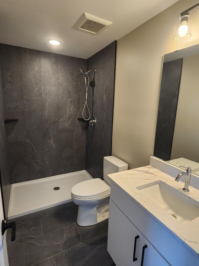 bathroom featuring vanity, toilet, a textured ceiling, and a tile shower