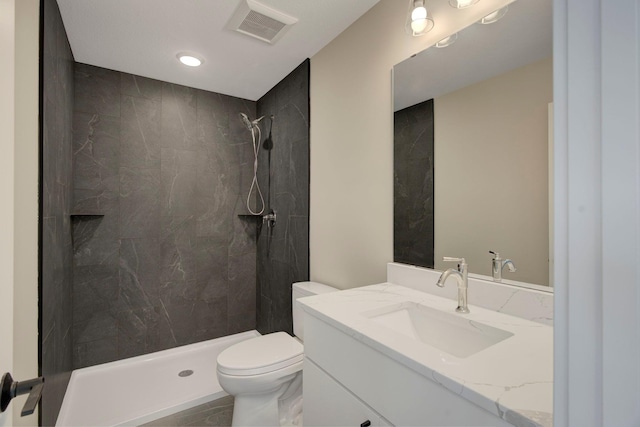 bathroom featuring vanity, a tile shower, and toilet