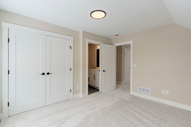 unfurnished bedroom featuring vaulted ceiling, light colored carpet, a closet, and ensuite bathroom