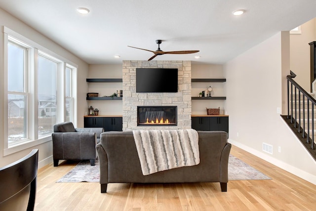 living room featuring ceiling fan, a stone fireplace, and light wood-type flooring