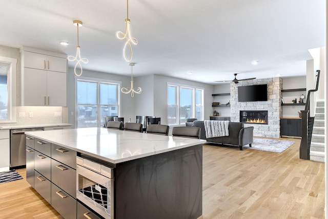 kitchen featuring light stone counters, decorative light fixtures, a kitchen island, stainless steel appliances, and light hardwood / wood-style floors