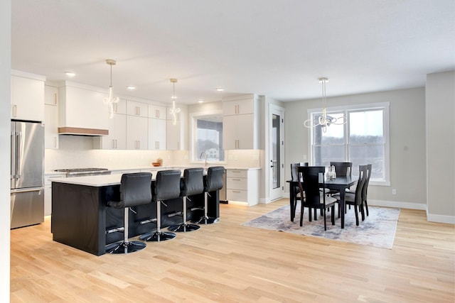 kitchen with hanging light fixtures, high quality fridge, white cabinets, a kitchen island, and custom exhaust hood