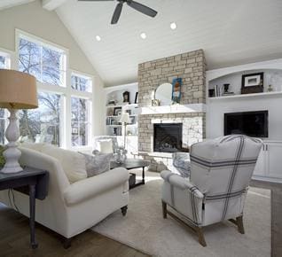 living room featuring hardwood / wood-style flooring, a stone fireplace, built in shelves, high vaulted ceiling, and ceiling fan