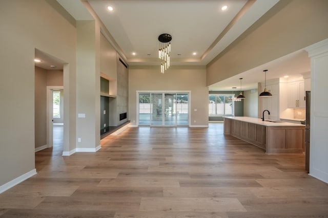 unfurnished living room featuring sink, light hardwood / wood-style flooring, a towering ceiling, and a healthy amount of sunlight