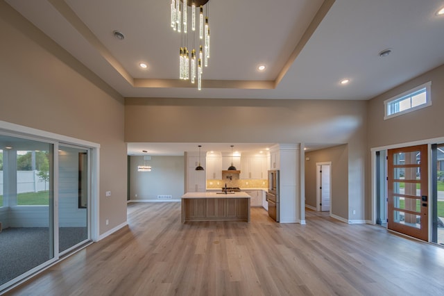 unfurnished living room featuring light hardwood / wood-style floors, sink, a healthy amount of sunlight, and an inviting chandelier