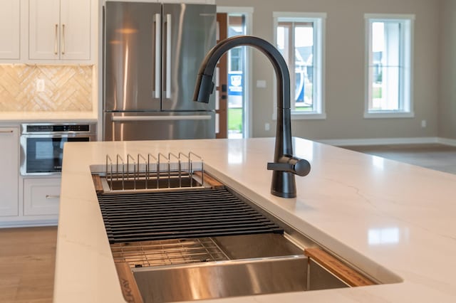 kitchen with backsplash, appliances with stainless steel finishes, light stone counters, and white cabinetry