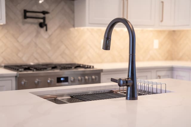 room details featuring white cabinetry, decorative backsplash, light stone counters, and sink