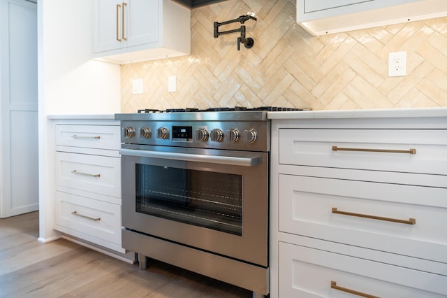 kitchen with high end stainless steel range oven, light hardwood / wood-style flooring, white cabinets, and backsplash