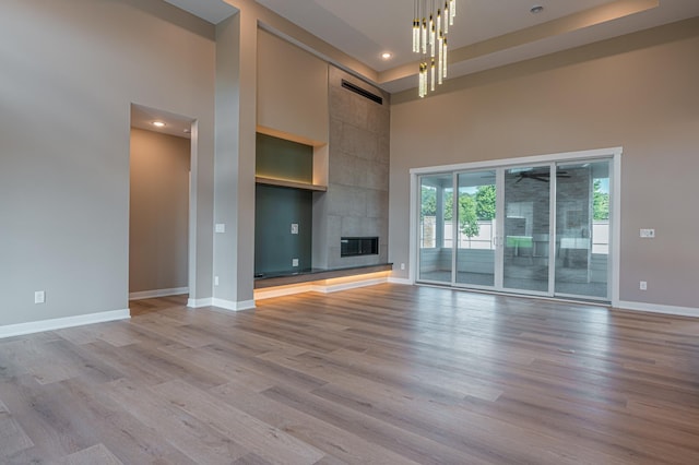 unfurnished living room with a high ceiling, an inviting chandelier, light hardwood / wood-style flooring, and a tiled fireplace