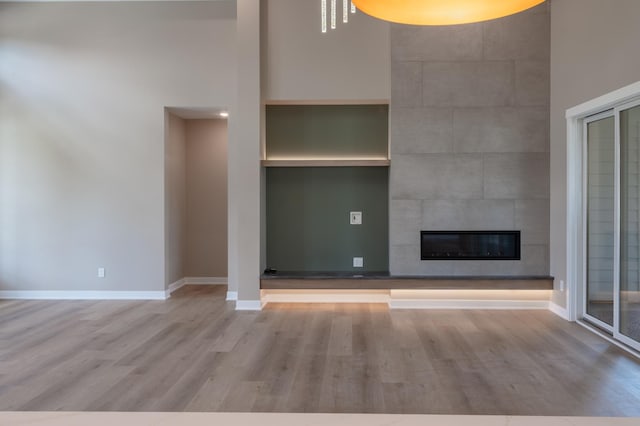 unfurnished living room with light wood-type flooring, a tiled fireplace, built in features, and a high ceiling