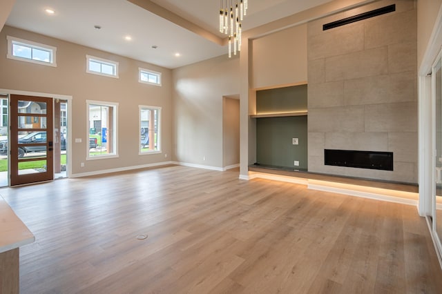 unfurnished living room featuring a high ceiling, built in shelves, a fireplace, a notable chandelier, and light wood-type flooring