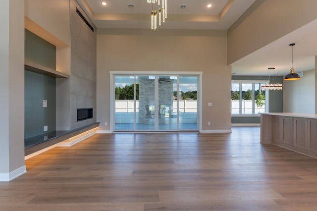 unfurnished living room featuring hardwood / wood-style flooring, a high ceiling, a tile fireplace, and a chandelier