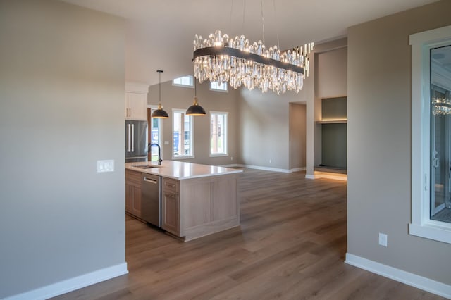 kitchen featuring sink, hanging light fixtures, a kitchen island with sink, appliances with stainless steel finishes, and a chandelier