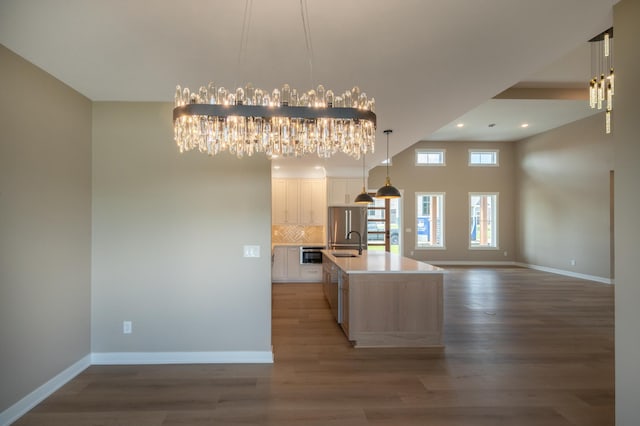 kitchen with a center island with sink, backsplash, a notable chandelier, white cabinets, and sink