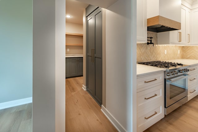 kitchen with white cabinetry, custom exhaust hood, high end stove, backsplash, and light wood-type flooring