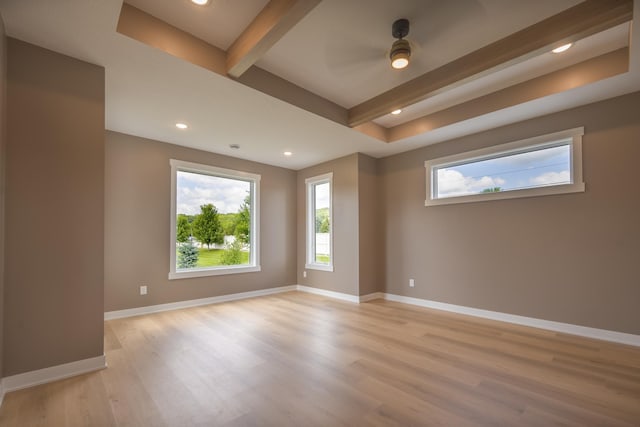 empty room featuring light wood-type flooring, ceiling fan, beam ceiling, and a tray ceiling