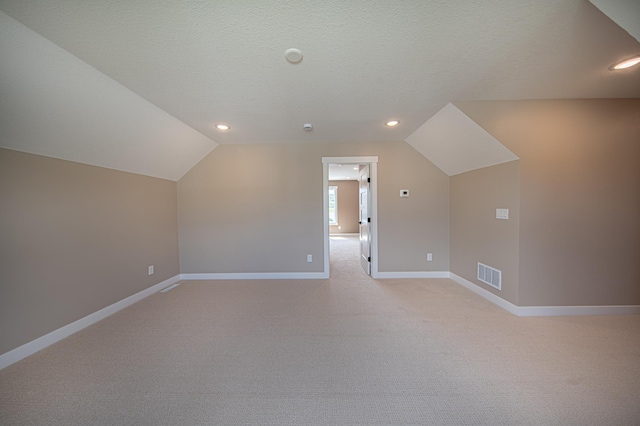 bonus room with lofted ceiling, light colored carpet, and a textured ceiling