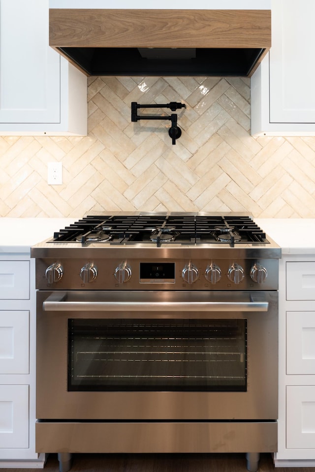 kitchen with exhaust hood, white cabinetry, gas range, and backsplash