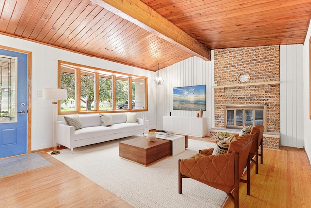 living room featuring brick wall, light wood-type flooring, a fireplace, vaulted ceiling with beams, and wooden ceiling