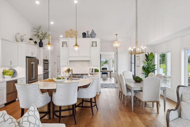 dining space featuring sink, high vaulted ceiling, a chandelier, and light wood-type flooring