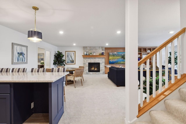 kitchen with light stone counters, a stone fireplace, hanging light fixtures, and light carpet