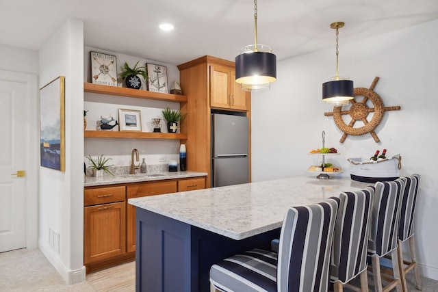 kitchen featuring light stone counters, stainless steel fridge, a kitchen bar, and hanging light fixtures