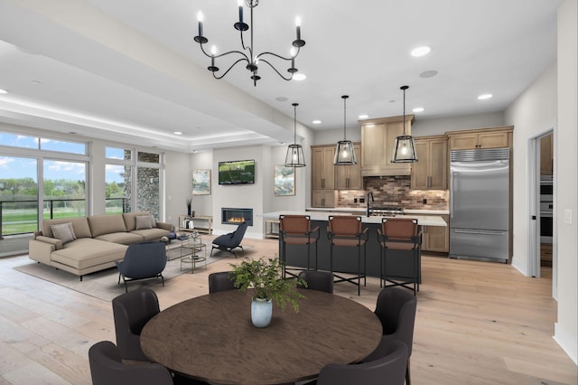 dining space with a tray ceiling, sink, light hardwood / wood-style flooring, and a notable chandelier