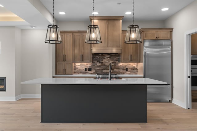 kitchen featuring stainless steel built in refrigerator, pendant lighting, light hardwood / wood-style floors, and an island with sink