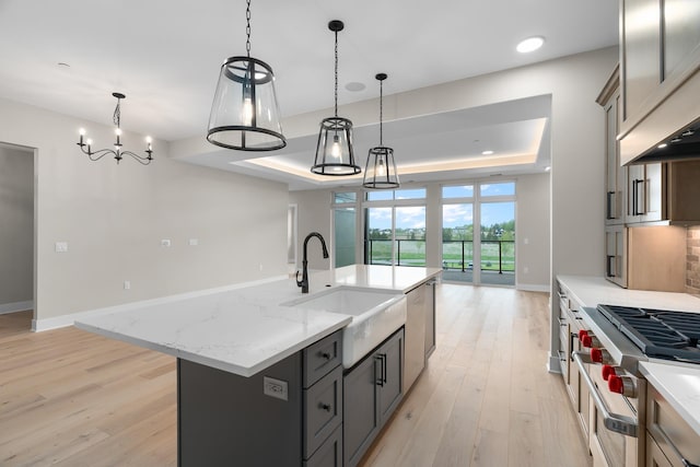 kitchen featuring a large island with sink, a raised ceiling, sink, decorative light fixtures, and stainless steel appliances