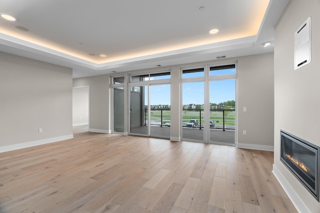 unfurnished living room with light wood-type flooring and a raised ceiling