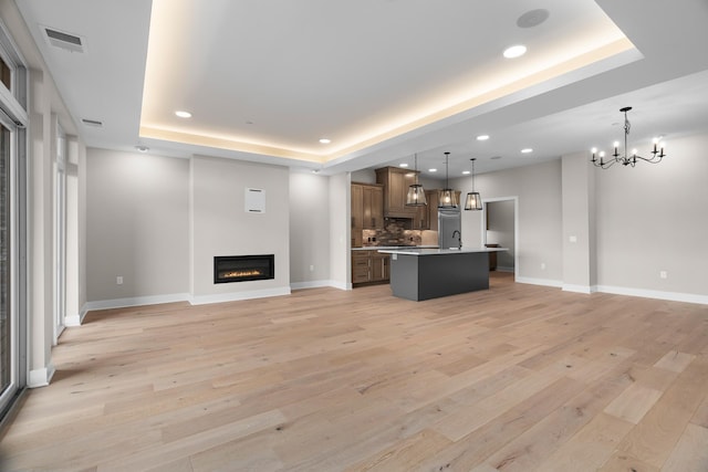 kitchen with light wood-type flooring, a raised ceiling, pendant lighting, an inviting chandelier, and a center island