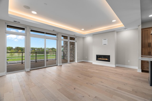 unfurnished living room featuring a tray ceiling and light wood-type flooring