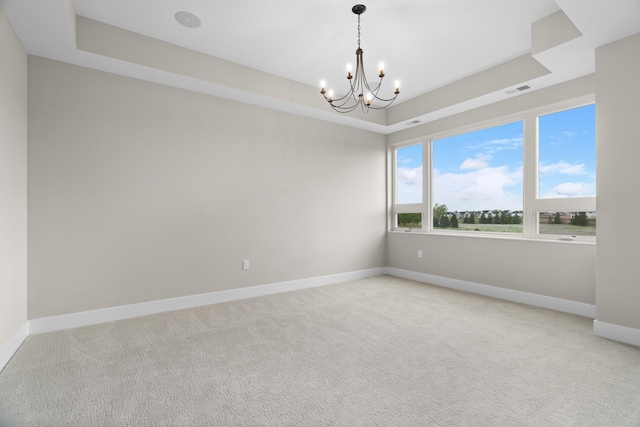 carpeted empty room with a notable chandelier and a raised ceiling