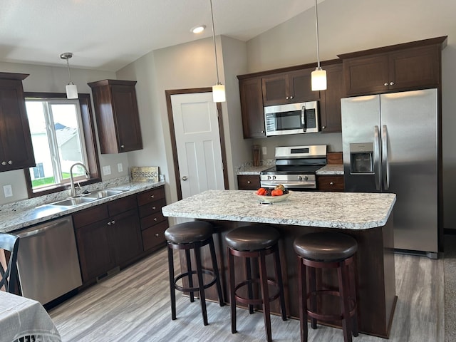 kitchen with appliances with stainless steel finishes, hanging light fixtures, a kitchen island, and sink