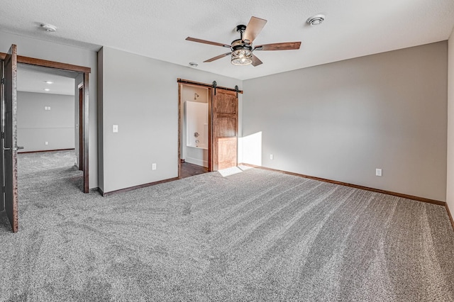 unfurnished bedroom with ceiling fan, connected bathroom, a textured ceiling, dark carpet, and a barn door