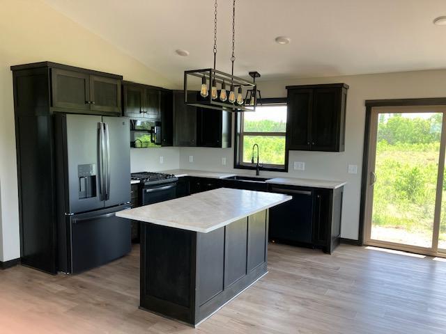 kitchen with sink, a center island, a wealth of natural light, black appliances, and decorative light fixtures