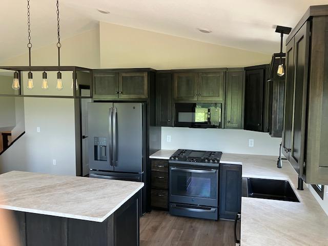 kitchen with appliances with stainless steel finishes, pendant lighting, lofted ceiling, and dark hardwood / wood-style flooring