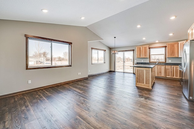 kitchen with pendant lighting, lofted ceiling, dark wood-type flooring, stainless steel refrigerator, and a center island