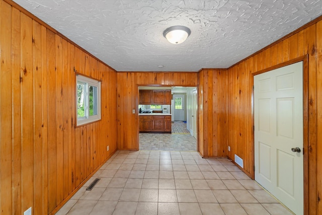 corridor featuring a textured ceiling, wooden walls, and crown molding