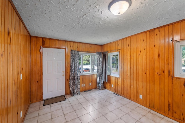 tiled empty room with ornamental molding, wood walls, and a textured ceiling