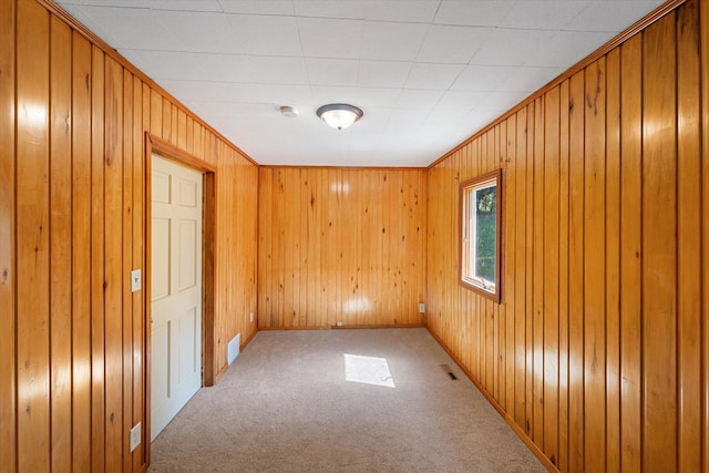 spare room with ornamental molding, wooden walls, and carpet flooring